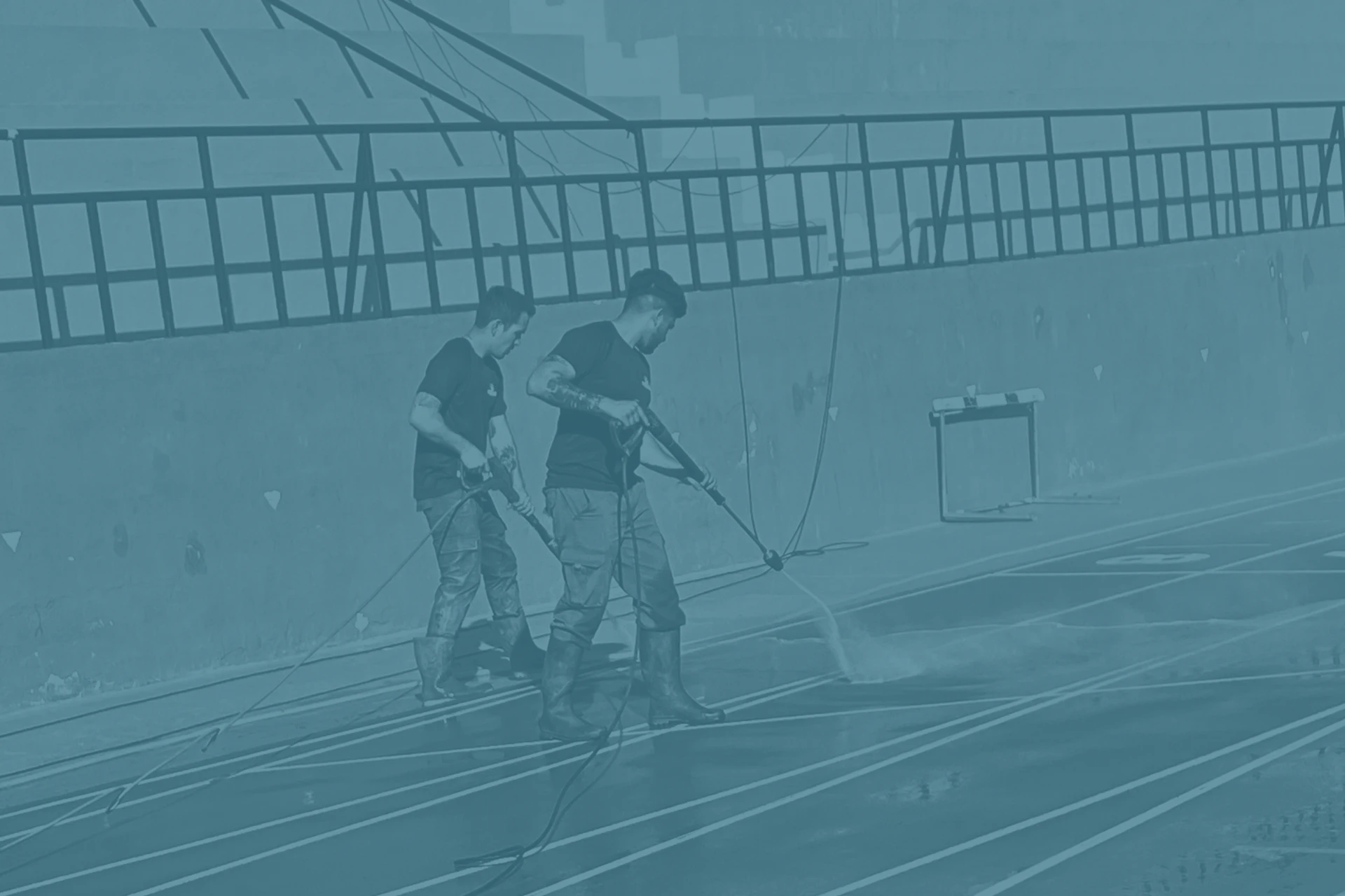 Imagen de dos trabajadores de Limpiezas Díaz limpiando una pista de atletismo con mangueras de agua a presión